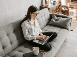 Young millennial woman writing on a couch with her laptop